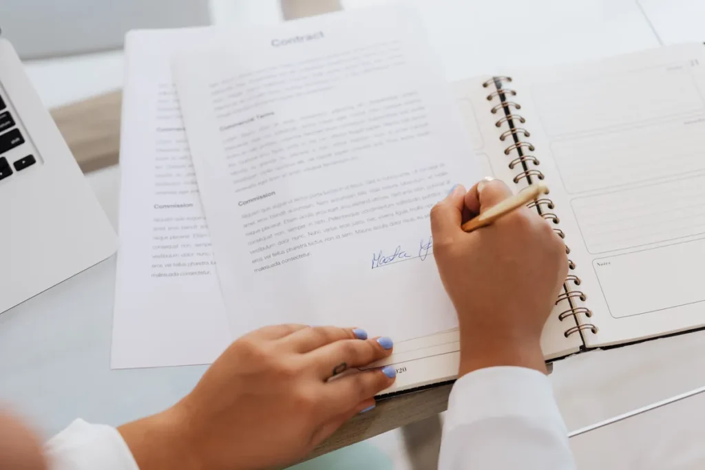 Tangan menandatangani surat perjanjian jasa hukum di atas meja kerja bersama tumpukan buku hukum